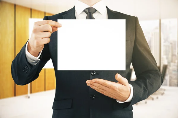 Close up of man in suit holding empty paper sheet in modern office interior. Mock up. Presentation concept