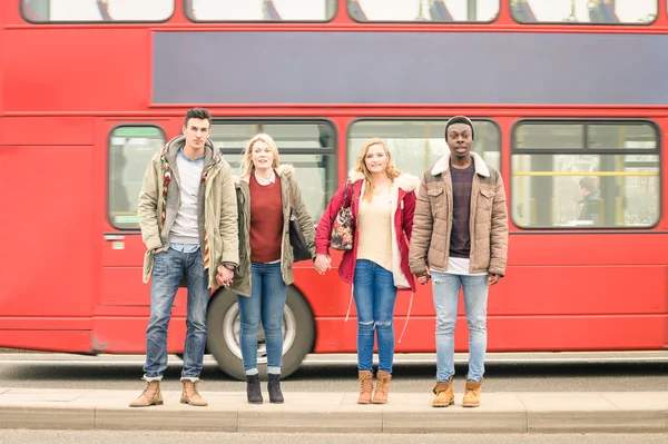 Group of fashion friends crossing the road with typical red bus behind - Autumn winter concept of social life with young people hanging out together - Neutral color tones with focus in guys and girls