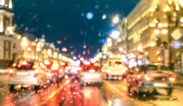 Defocused abstract rush hour with rain drops at night - Bokeh of moving cars stuck in traffic jam on Nevsky Prospekt in Saint Petersburg at blue hour - Blurred postcard on warm vivid filtered look
