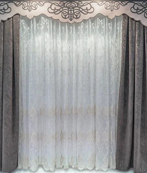 The straight, brown curtains of the dense natural material, a light tulle organza, hard pelmet with a pattern