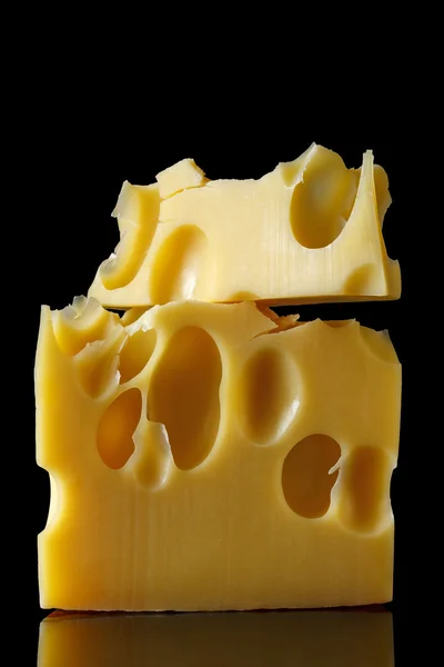 A piece of Swiss cheese with large holes on a black background with reflection. minimalist style of food art. cheese closeup