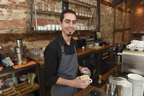 Young italian barista or coffee maker at restaurant shop preparing milk cream at cafe machine