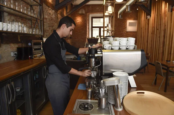 Young italian barista or coffee maker at restaurant shop preparing milk cream at cafe machine