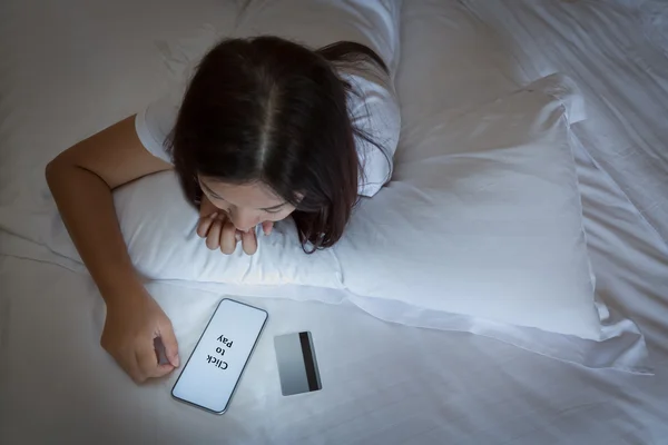 Asian woman using smartphone and credit card on bed,Woman enjoy shopping online with smartphone and credit card on bed at night time