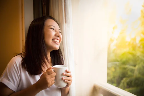 Asian girl hold cup of coffee relaxing look outside window