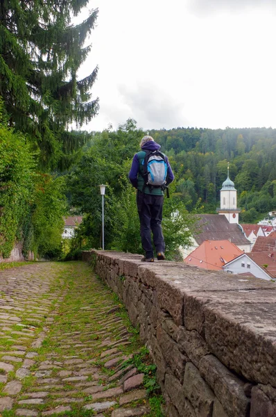 Man with backpack walking over small wall on the side of a street