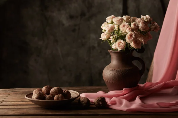 Still life with roses and walnuts on the table with pink fabric