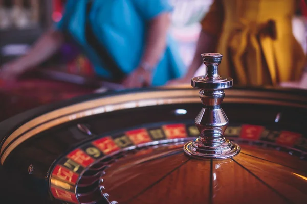 A close-up vibrant image of multicolored casino table with roulette in motion, with the hand of croupier, and a group of gambling rich wealthy people