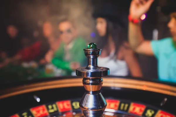 A close-up vibrant image of multicolored casino table with roulette in motion, with the hand of croupier, and a group of gambling rich wealthy people
