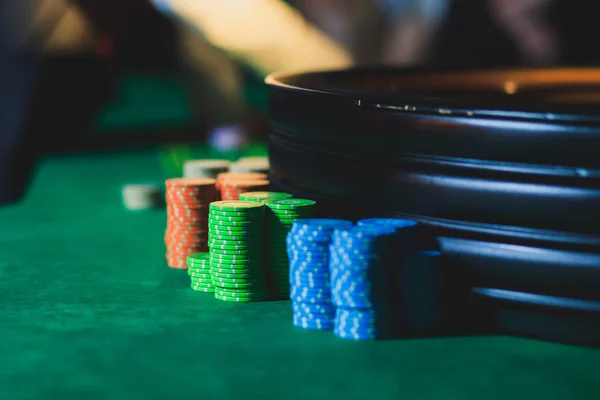 A close-up vibrant image of multicolored casino table with roulette in motion, with the hand of croupier, and a group of gambling rich wealthy people