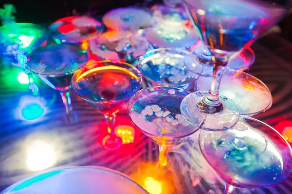 Beautiful row line of different colored alcohol cocktails with mint on a open air party, martini, vodka with bubbles,and others on decorated catering bouquet wedding table on open air event, in nigh