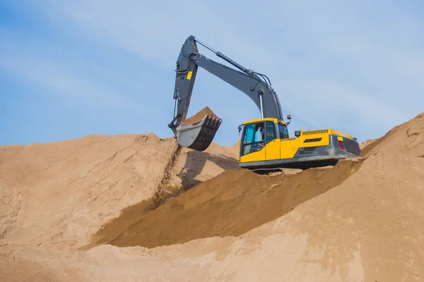 Yellow heavy excavator and bulldozer excavating sand and working during road works, unloading sand and road metal during construction of the new road