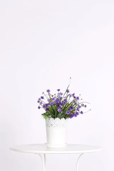 White pot with artificial flowers on table on light background