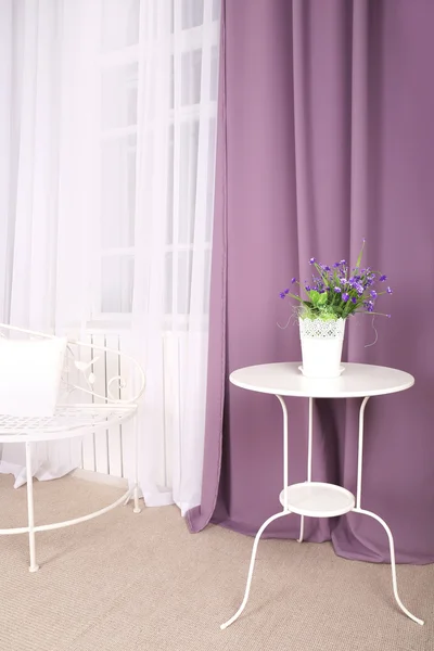 White table with flower in the room on background of purple curtains