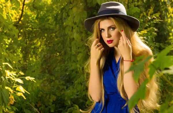 girl with long hair in a hat and blue dress posing in autumn fo