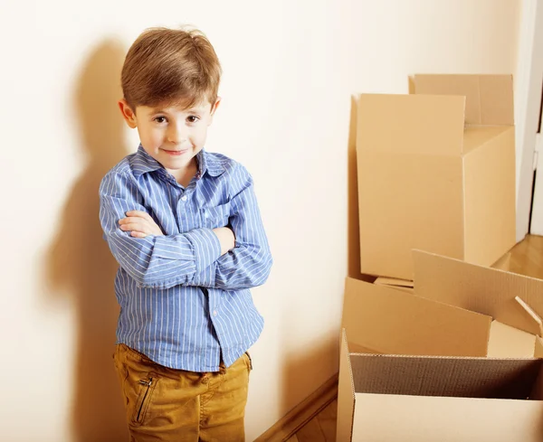 Little cute boy in empty room, remoove to new house. home alone among boxes close up smiling kid, lifestyle people concept