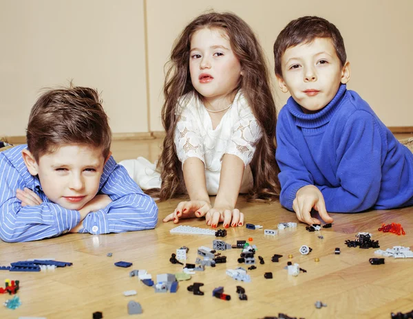 Funny cute children playing lego at home, boys and girl smiling, first education role close up on floor