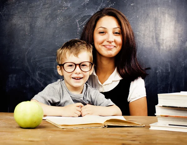 Little cute boy with young teacher in classroom studying at blackboard smiling, lifestyle people concept