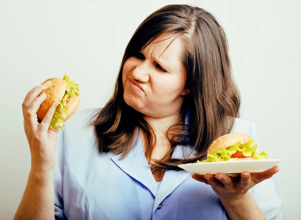 Fat white woman having choice between hamburger and salad, eating emotional unhealthy food, lifestyle people concept