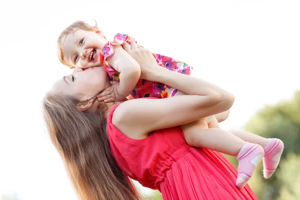 Mother kissing baby daughter in pink dress,