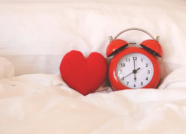 Red alarm Clock and heart shape on white bed sheet