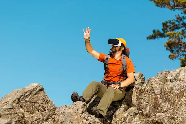 Successful young man, using virtual reality goggles to tour in mountains, on vacation in summer