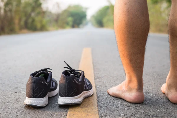 Legs of man with black running shoes on asphalt road in morning