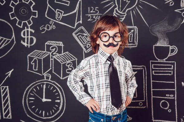 Little boy as businessman or teacher with mustache and glasses standing on a dark background pattern. Wearing shirt, tie