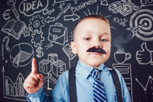 Little boy as businessman or teacher with mustache standing on dark background pattern. Wearing shirt and tie. Lifting a finger up