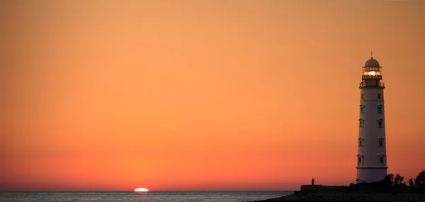 Lighthouse searchlight beam near ocean at sunset