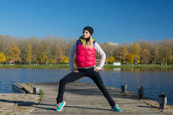A beautiful girl with a slim figure in the black leggings and bright pink jacket is playing sports  in the autumn park in sunny weather.