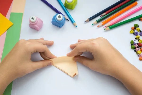 Children\'s hands do origami  wolf  from peach paper.