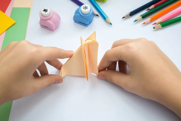 Children\'s hands do origami  wolf  from peach paper.