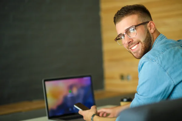 Young man using phone and works on the laptop