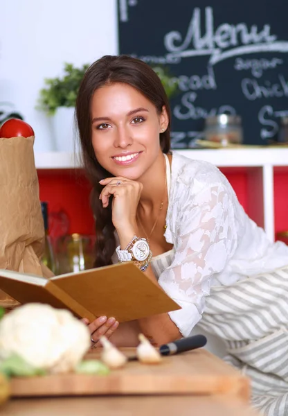 Young woman reading cookbook in the kitchen, looking for recipe