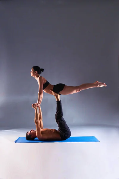 Young couple practicing acro yoga on mat in studio together