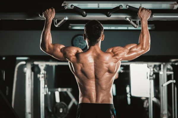 Athlete muscular fitness male model pulling up on horizontal bar in a gym