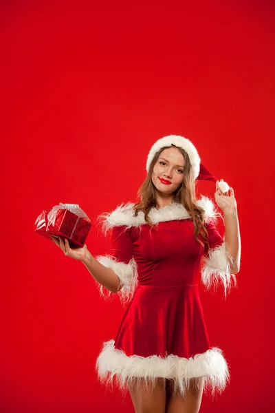 Christmas, x-mas, winter, happiness concept - smiling woman in santa helper hat with gift box, over red background