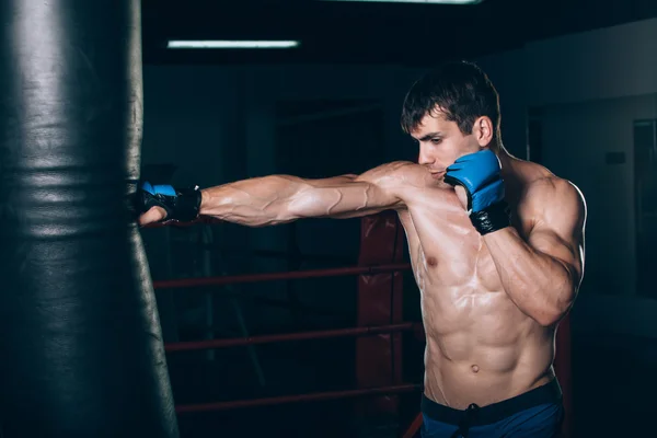 Young Male boxer using a punching bag in gym.