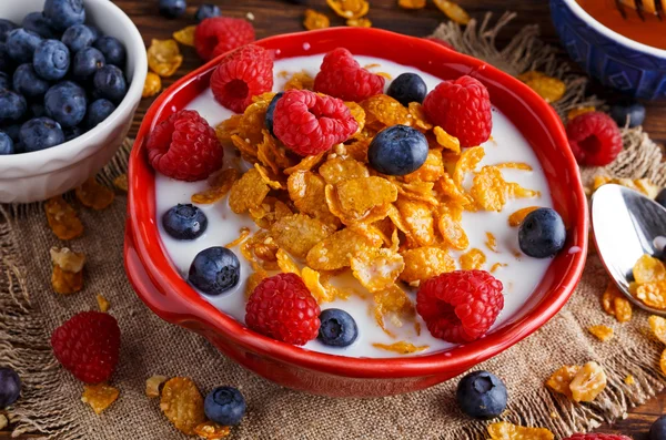 Corn Flakes with berries raspberries, blueberries, glass of milk, and sweet honey.