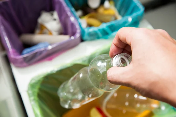 Man putting empty plastic bottle in recycling bin in the kitchen.