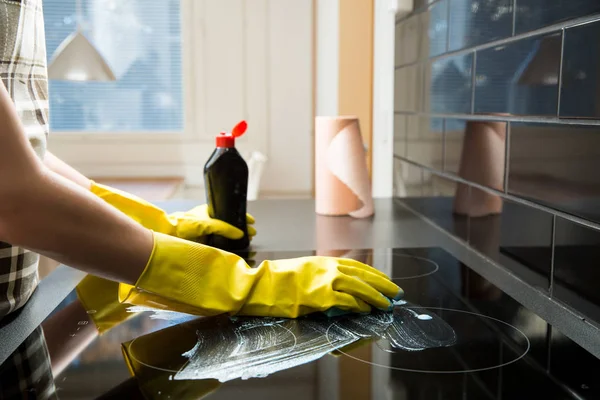 Housewife in rubber protective cleaning and polish electric cooker