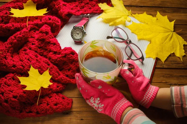 Hands holding a cup of tea on the old wooden table, autumn compo