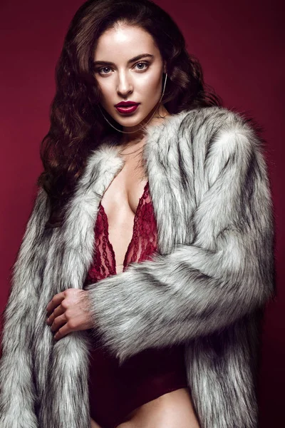Beautiful sexy long-haired brunette woman in red lingerie and fur coat. beauty face, body.