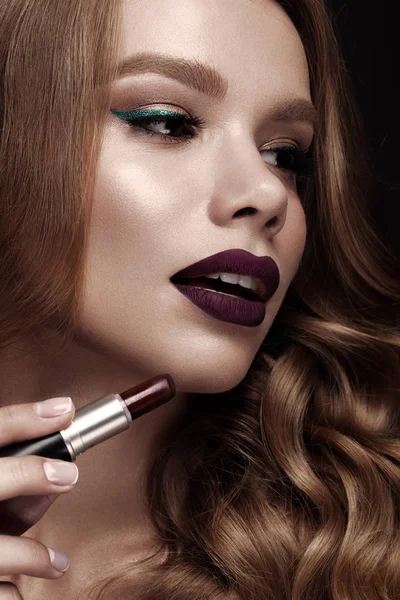 Beautiful blonde in a Hollywood manner with curls, dark lips, lipstick in hand. Beauty face and hair.