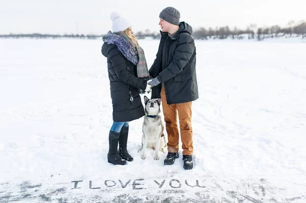 Happy couple standing with a dog in winter park. Declaration of love on St. Valentine\'s Day.