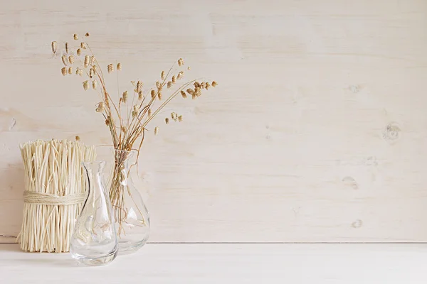 Soft home decor of  glass vase with spikelets and stalks on white wood background.