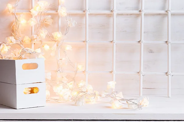 Christmas soft home decor with lights burning and boxes on a white wooden background.