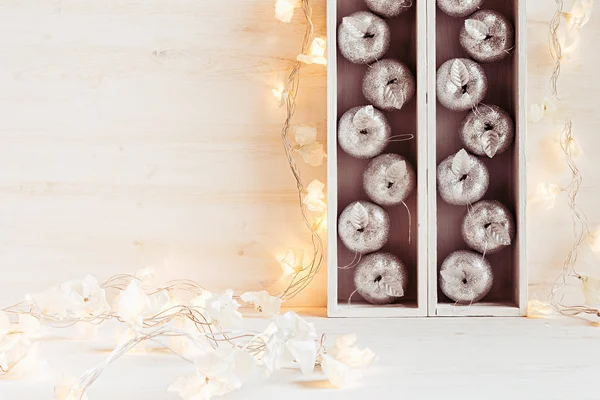 Christmas soft home decor of silver apples and lights burning in boxes  on a wooden white  background.