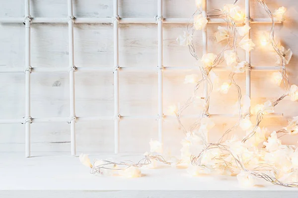 Christmas soft home decor with lights burning  on a white wooden background.